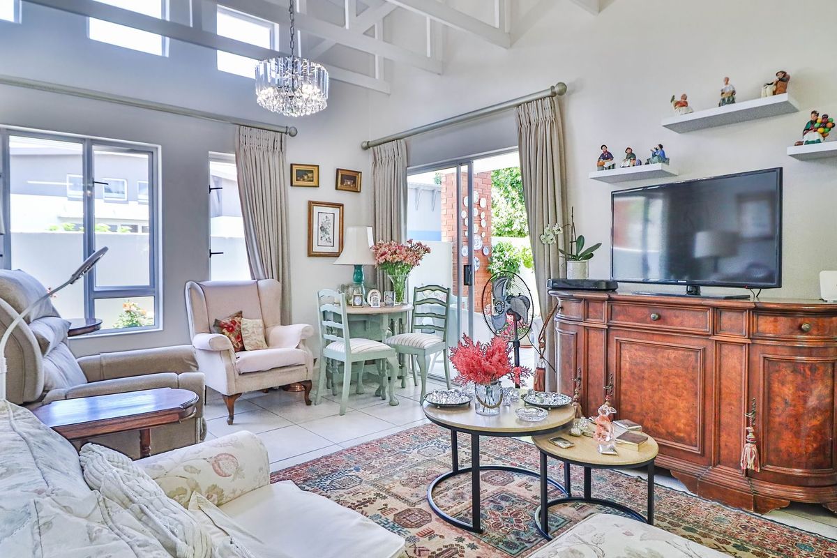 A bright living room featuring a high vaulted ceiling with exposed rafters, tiled flooring, and large sliding glass doors leading to an outdoor area.