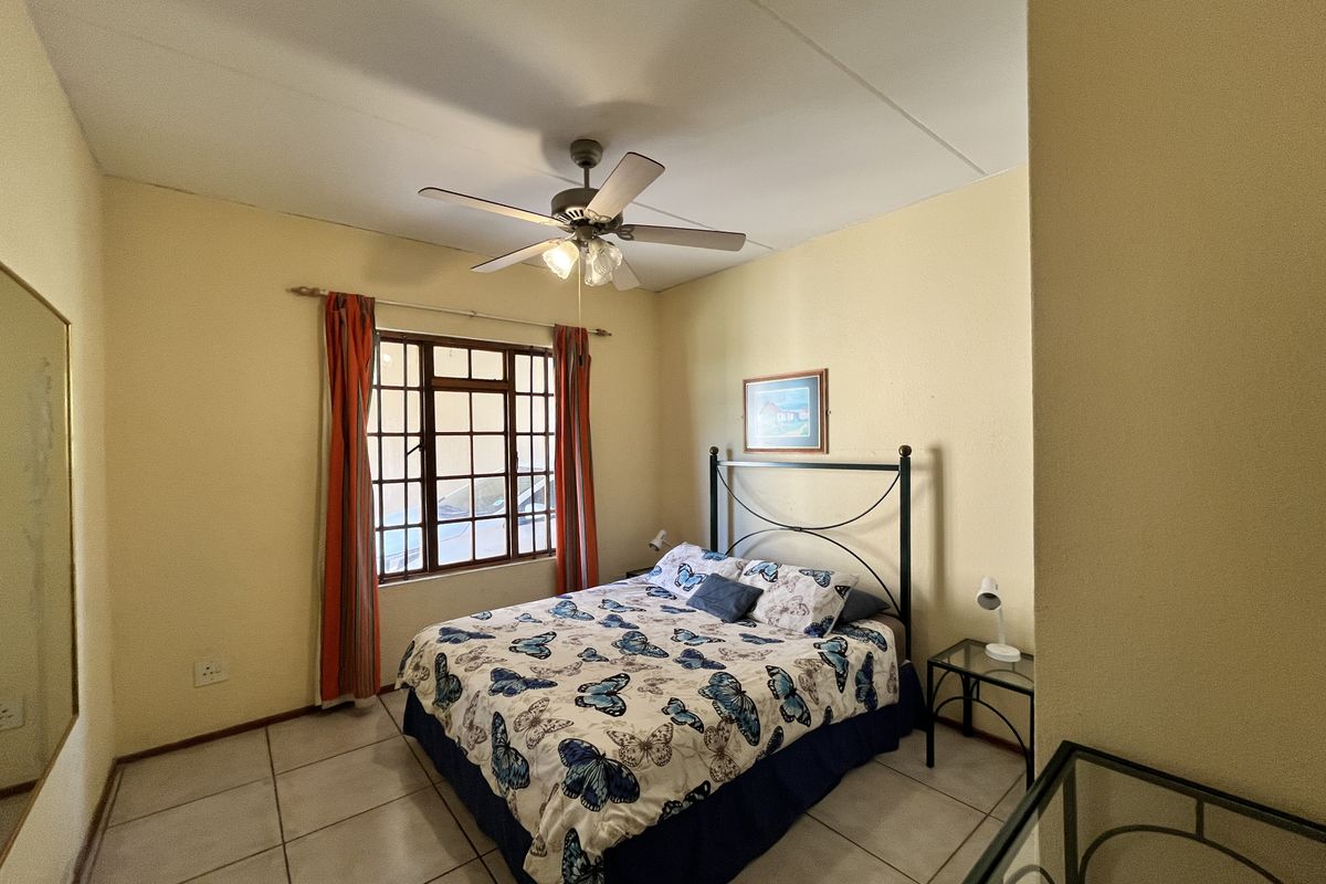 A bedroom featuring tiled flooring, a ceiling fan, and a window with security bars, providing a functional and well-lit sleeping space.