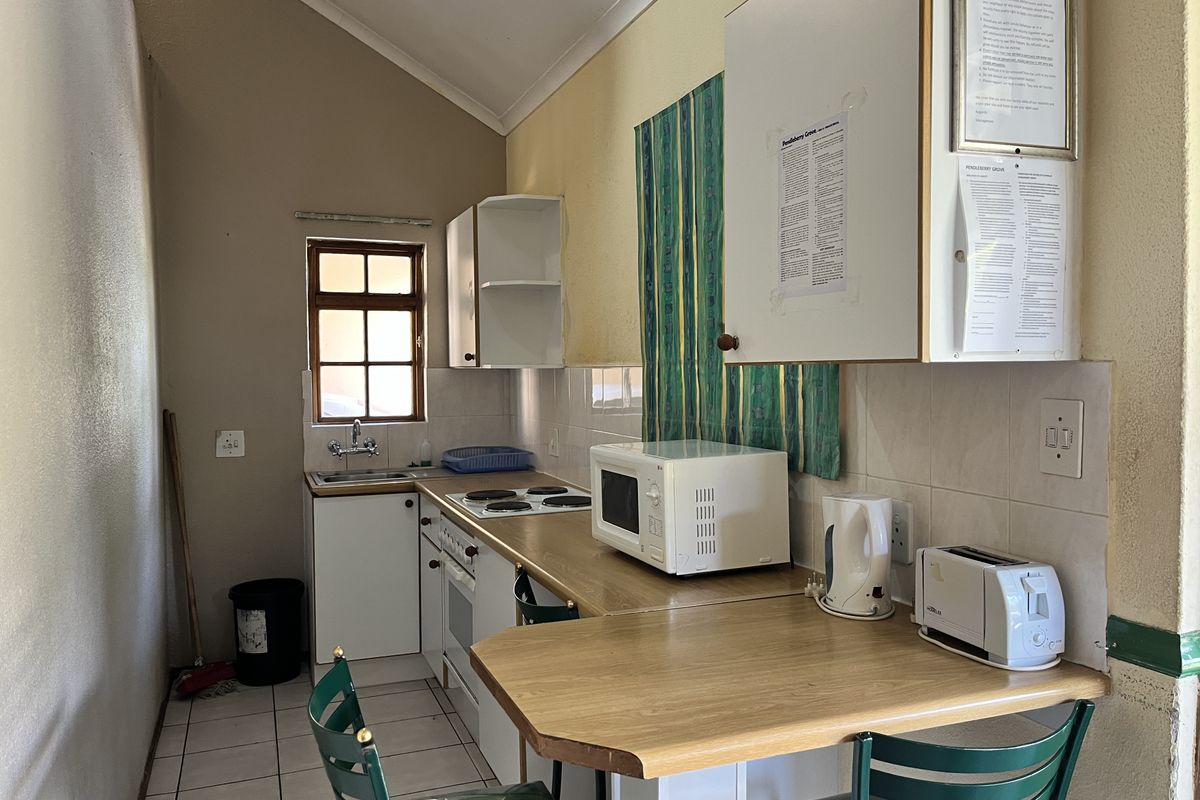 A compact, functional kitchen featuring built-in cabinetry, a laminate countertop, an electric hob, and a stainless steel sink with tiled splashbacks.