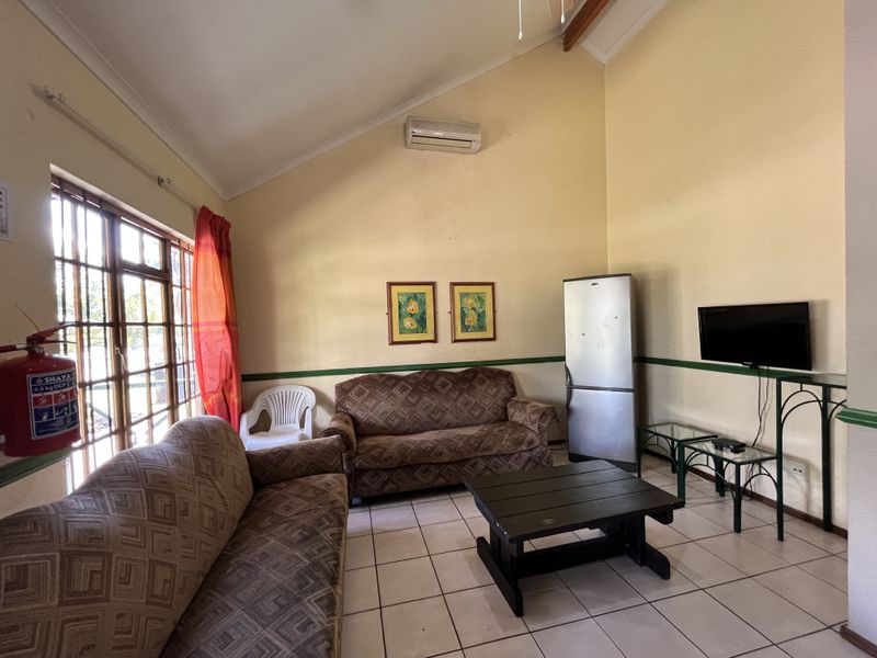 A living room featuring vaulted ceilings, tiled flooring, and a wall-mounted air conditioning unit, offering a functional space with potential for cosmetic updates.