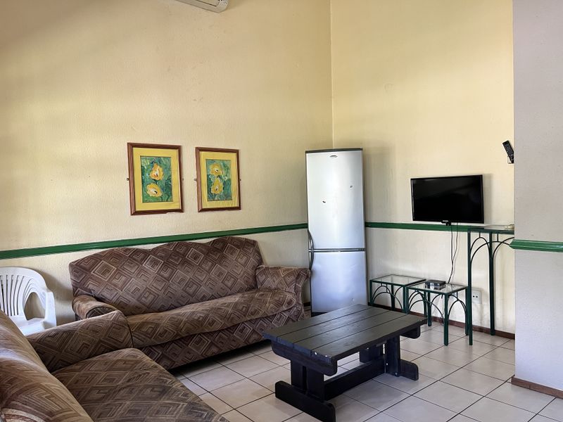 A living room area featuring tiled flooring, chair rail molding, and a wall-mounted air conditioning unit, presenting a dated aesthetic in need of cosmetic updates.