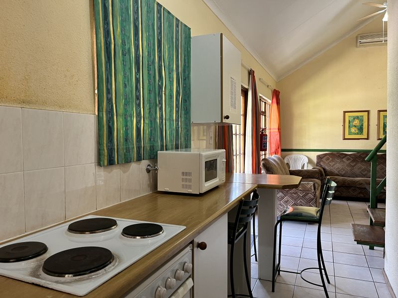 Open-plan living area featuring a functional kitchen with electric hob, breakfast bar, and tiled flooring, leading into a comfortable lounge space.