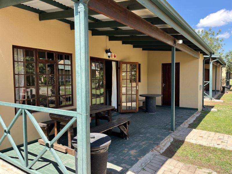 A covered outdoor patio area featuring paved flooring, timber-framed doors and windows, and a sheltered seating space overlooking the garden.