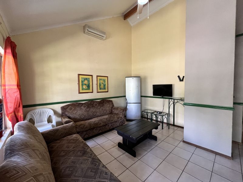 A living room featuring vaulted ceilings, ceramic tiled flooring, and a wall-mounted air conditioning unit.