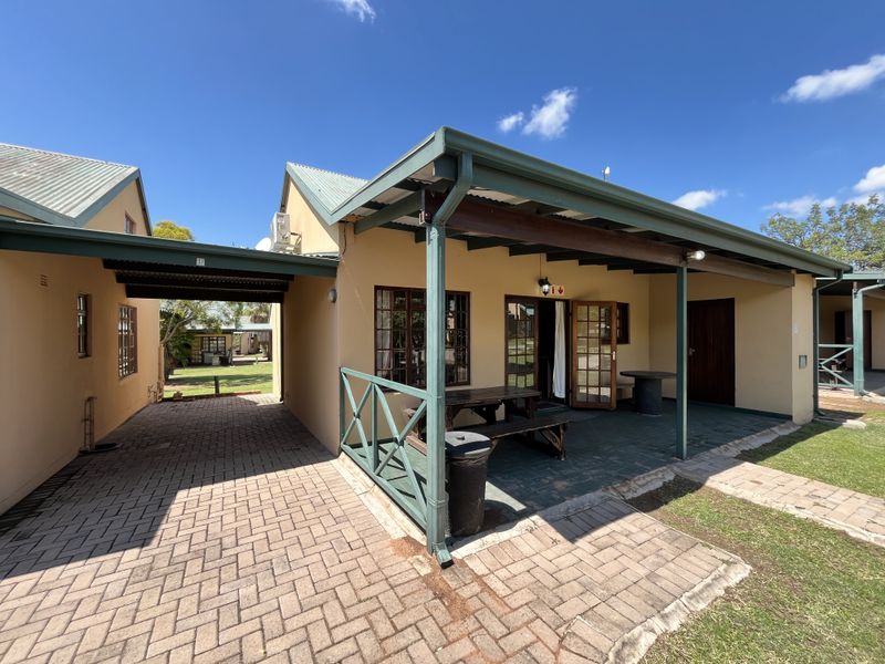 Rear view of the property featuring a covered patio area, paved driveway, and well-maintained exterior walls with timber accents.