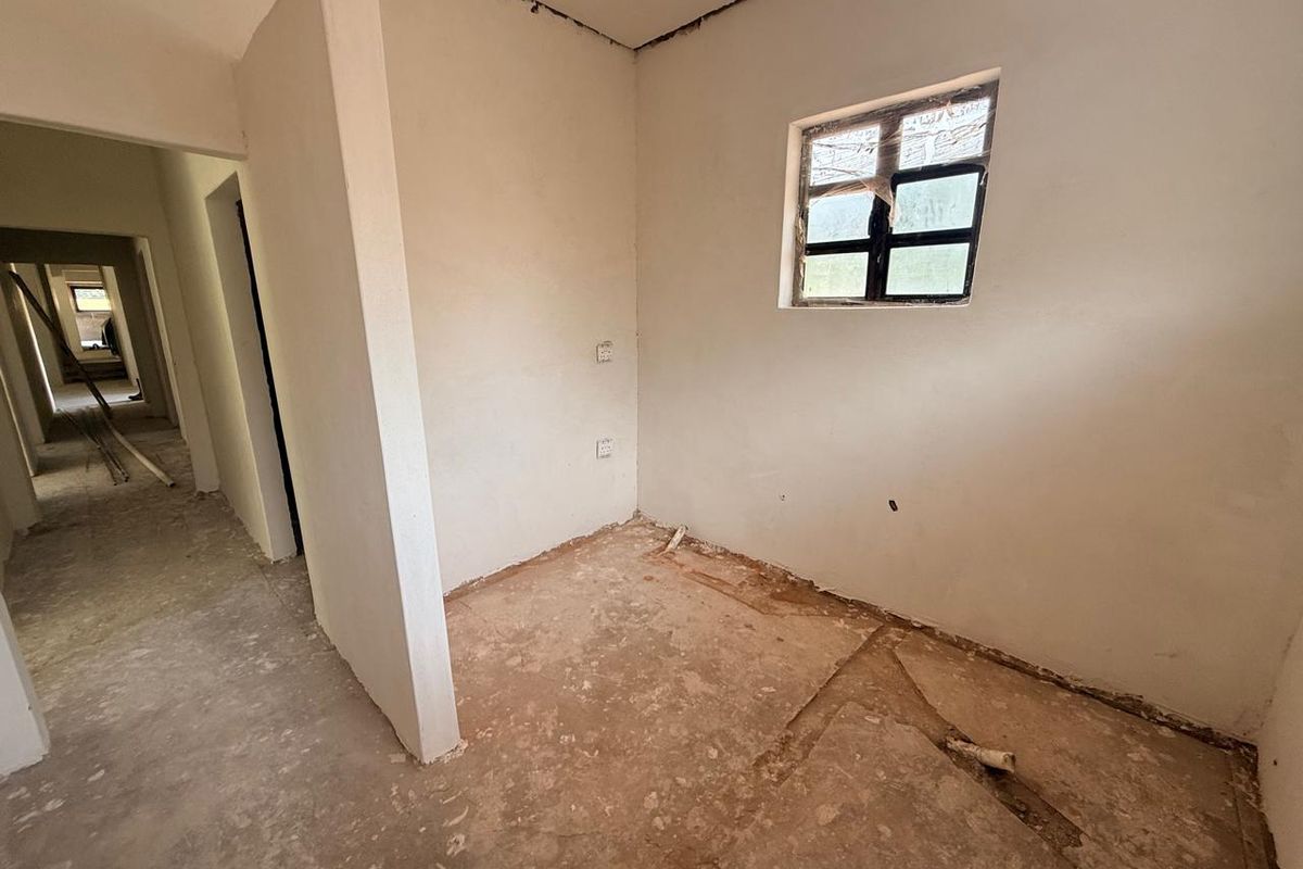 An unfinished interior room in shell condition, featuring exposed concrete flooring, plastered walls, and a small window, currently undergoing renovation.