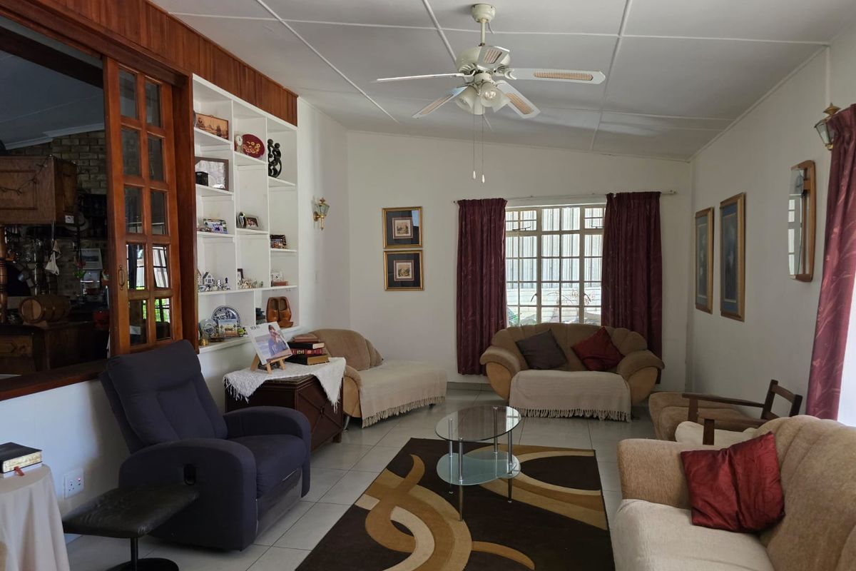 A spacious living room featuring built-in shelving, a ceiling fan, and large windows that provide natural light.
