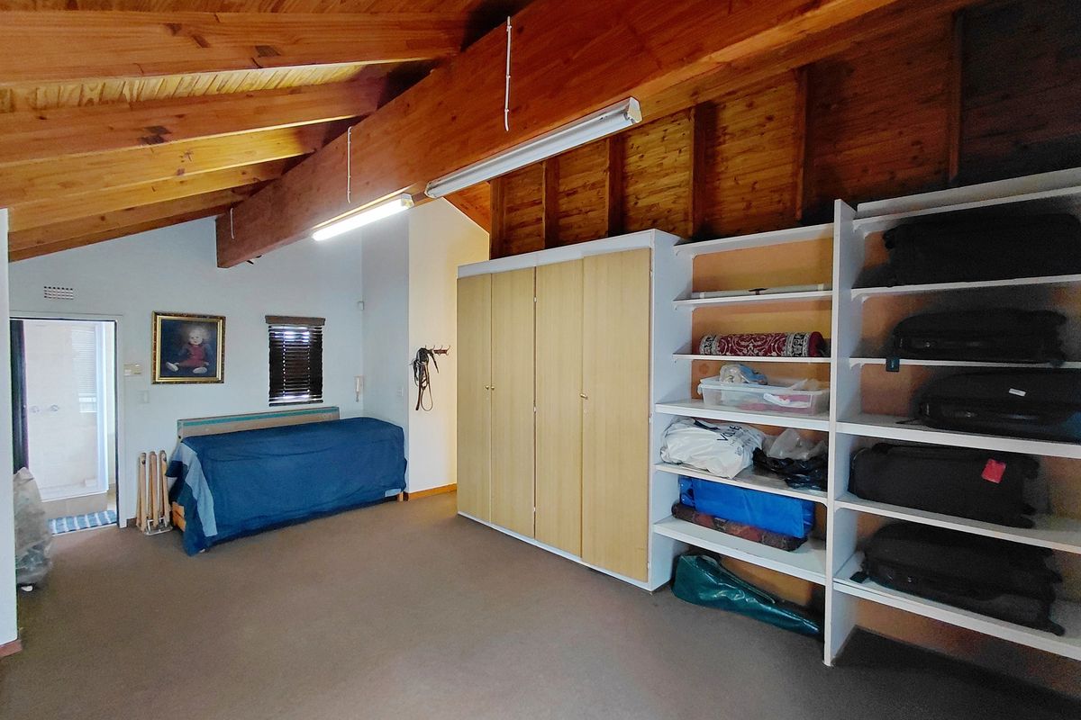 A spacious room featuring exposed timber beams, vaulted ceilings, built-in cabinetry, and open shelving, providing versatile storage or living space.