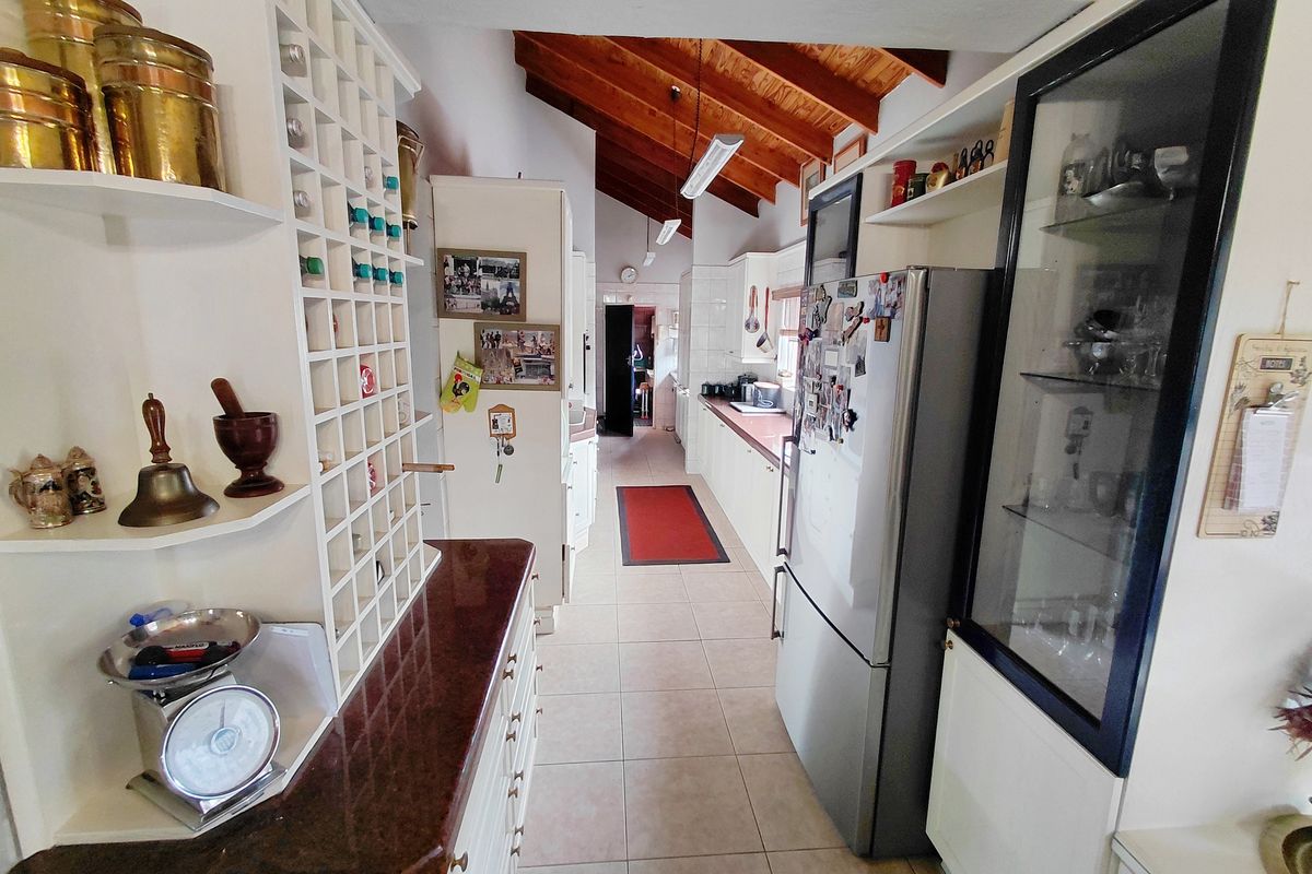 A long, galley-style kitchen featuring white cabinetry, stone countertops, tiled flooring, and an exposed timber beam ceiling.