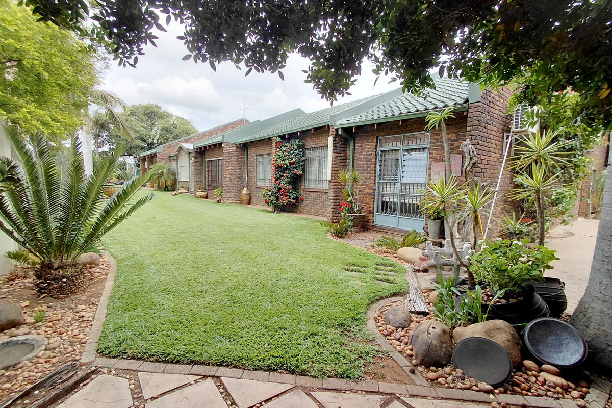 A view of the rear exterior of the house featuring a well-maintained lawn, landscaped garden beds, and paved pathways along the brick facade.