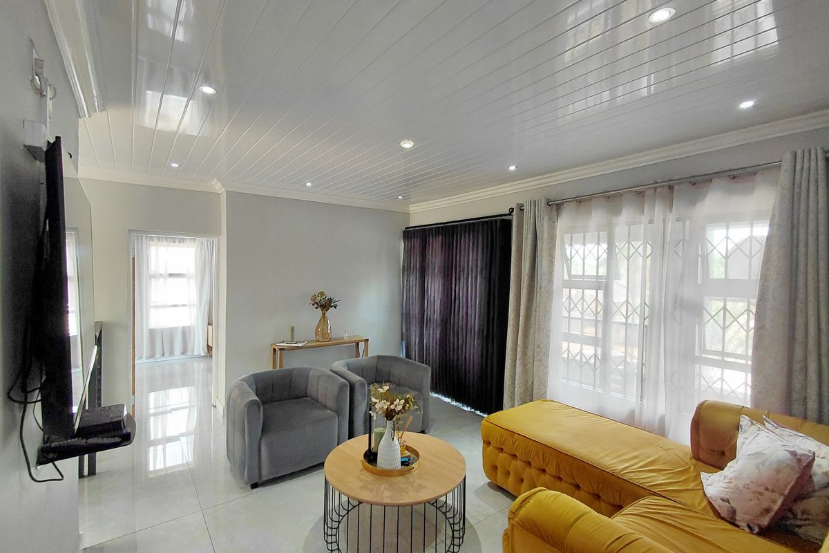 A bright living room featuring polished floor tiles, recessed ceiling lighting, and large windows with security gates, offering a clean and modern living space.