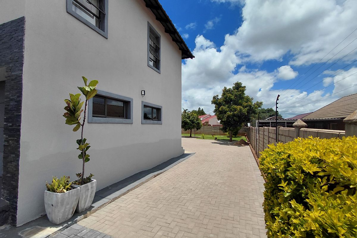 Side view of the property featuring paved driveway, exterior wall cladding, and perimeter boundary wall with electric fencing.