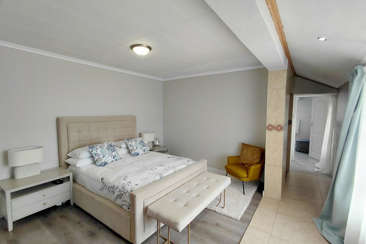 A spacious bedroom featuring light-toned laminate flooring, neutral walls, and a tiled transition area leading to an adjacent room.