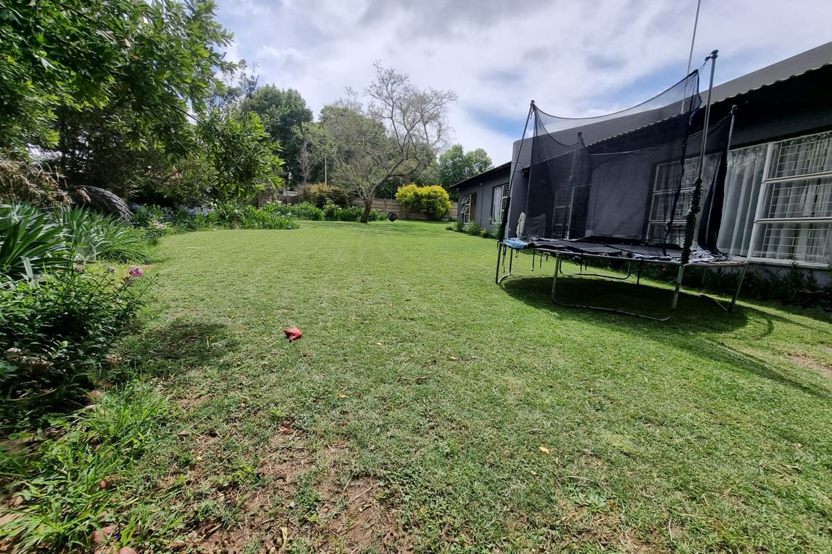 A spacious rear garden featuring a well-maintained lawn, mature trees, and a view of the property's rear exterior facade.