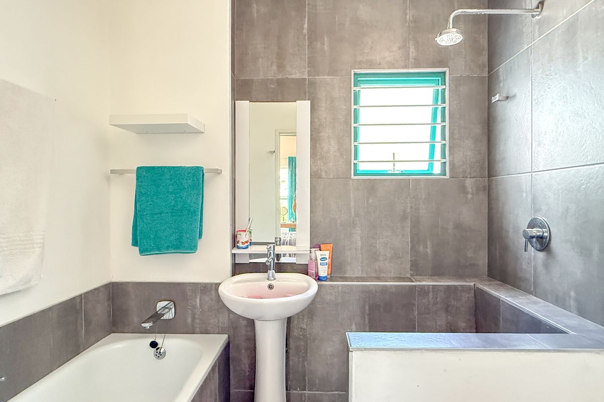 Modern bathroom featuring a pedestal sink, built-in bathtub, and a walk-in shower area with grey wall tiling and a small ventilation window.