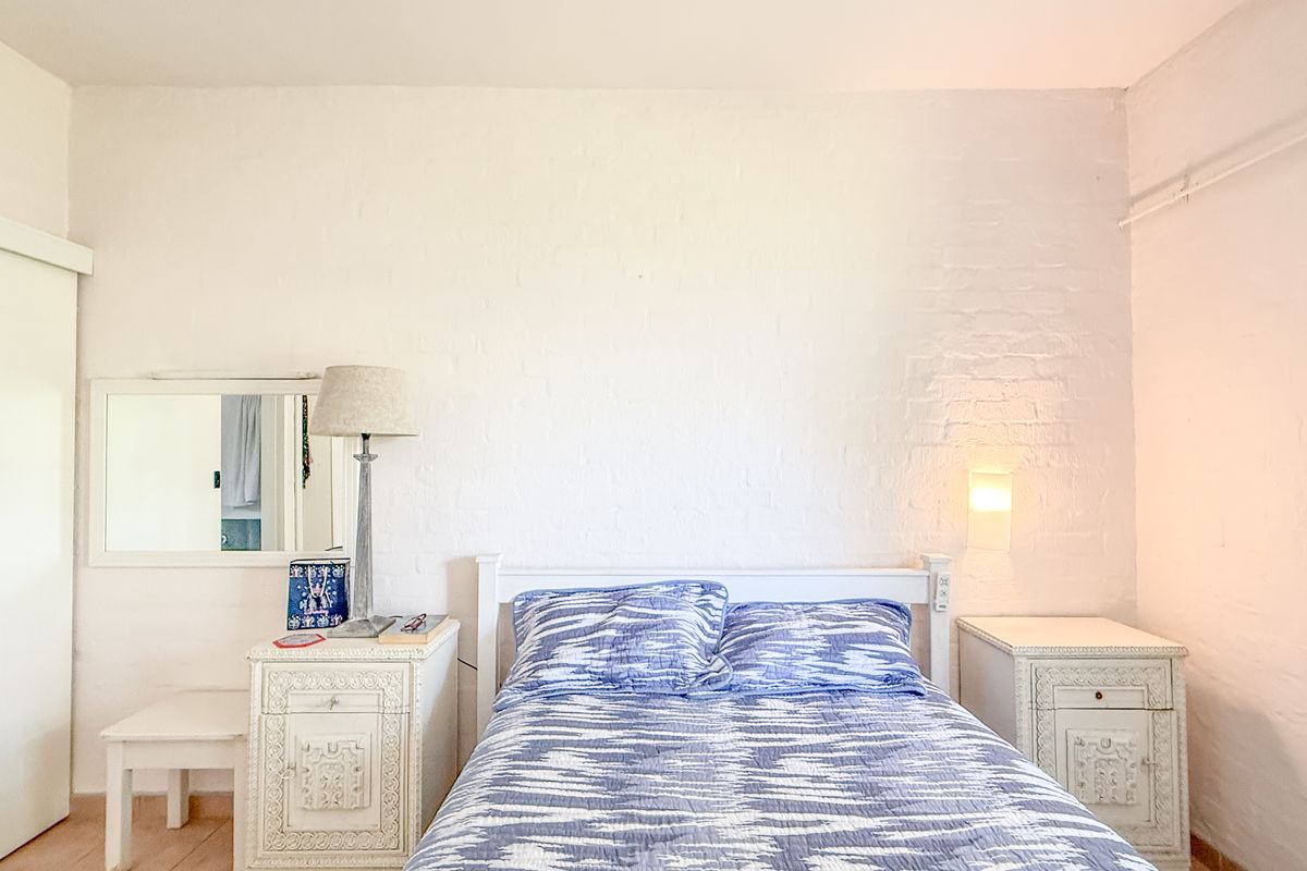 A bedroom featuring a painted brick feature wall, built-in sliding door wardrobe, and wall-mounted lighting fixtures.