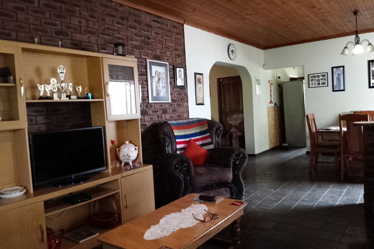 A living area featuring a rustic exposed brick feature wall, dark slate flooring, and a timber-paneled ceiling, leading into an adjacent dining space.