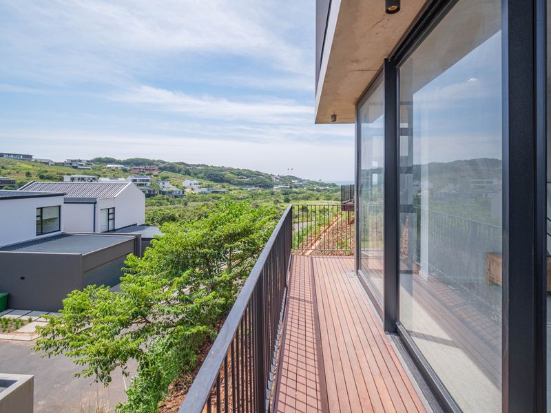A modern balcony featuring timber decking and a sleek metal balustrade, offering expansive views of the surrounding landscape and neighborhood.