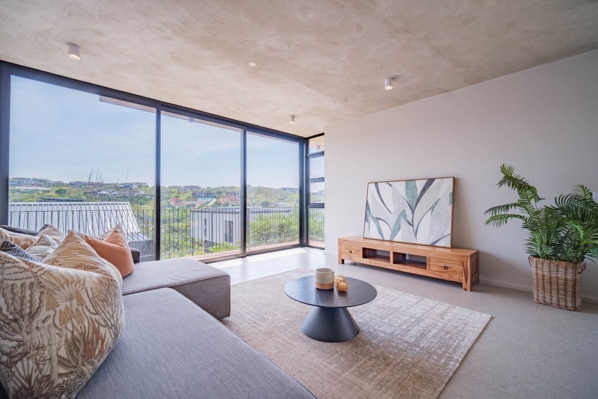 Modern living room featuring an exposed concrete ceiling, large floor-to-ceiling sliding glass doors, and expansive views of the surrounding landscape.