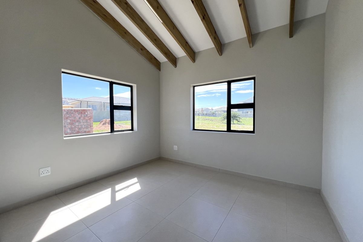 A bright, empty bedroom featuring vaulted ceilings with exposed timber beams, neutral tiled flooring, and modern black-framed windows.