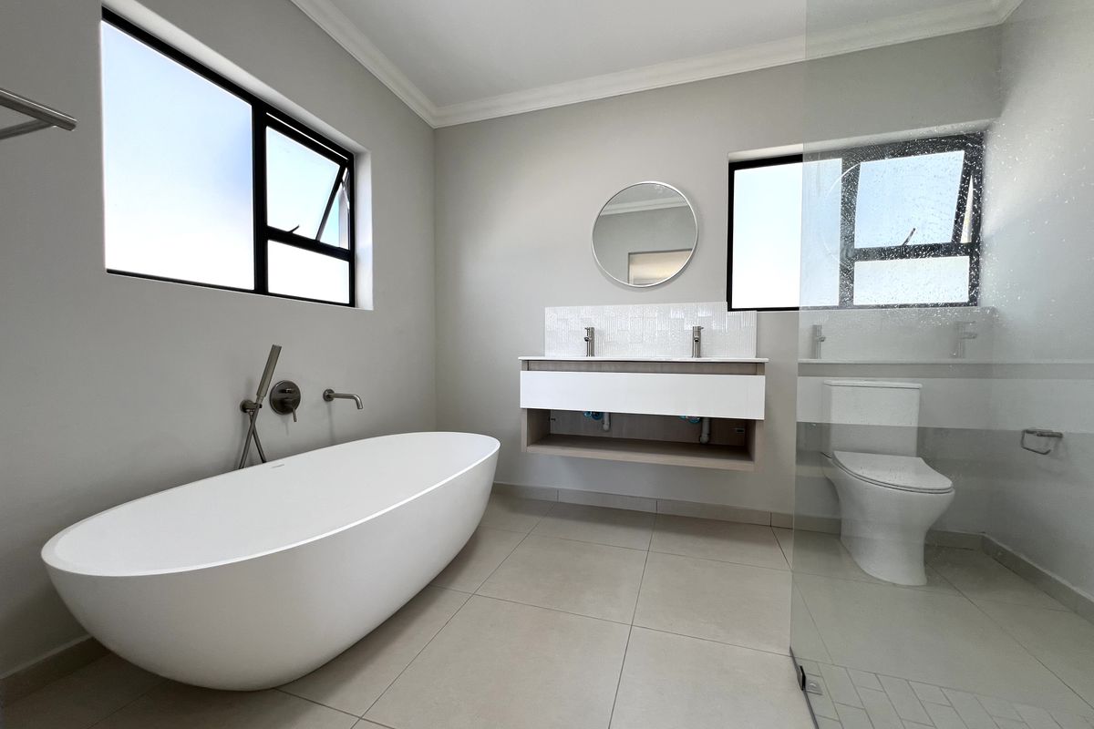 Modern bathroom featuring a freestanding bathtub, wall-mounted double vanity, and a glass-enclosed toilet area with large format floor tiles.