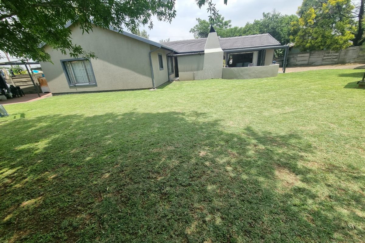 Spacious rear garden featuring a well-maintained lawn, exterior building facade, and a prominent outdoor fireplace structure.