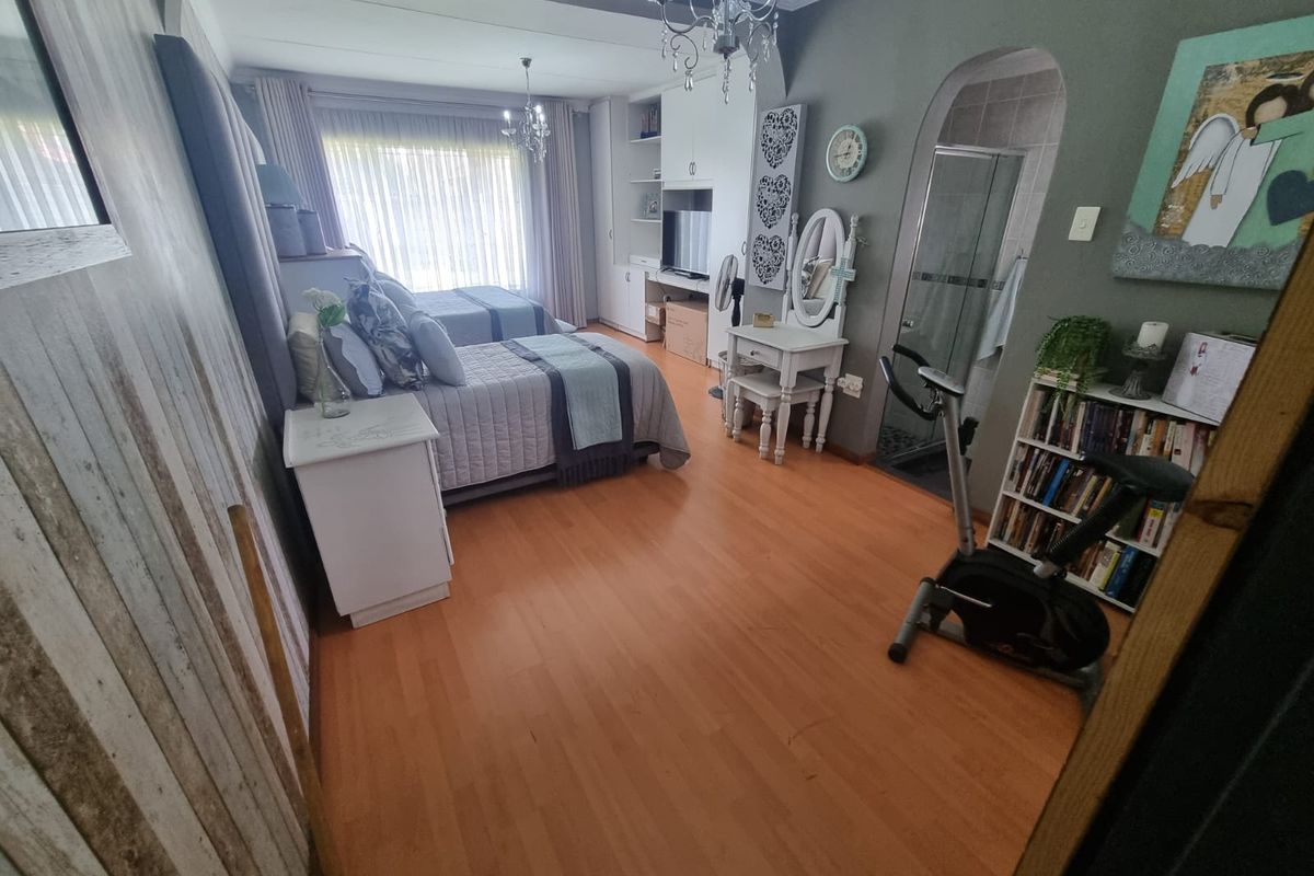 Spacious bedroom featuring laminate flooring, built-in cabinetry, and an en-suite bathroom with a glass-enclosed shower.