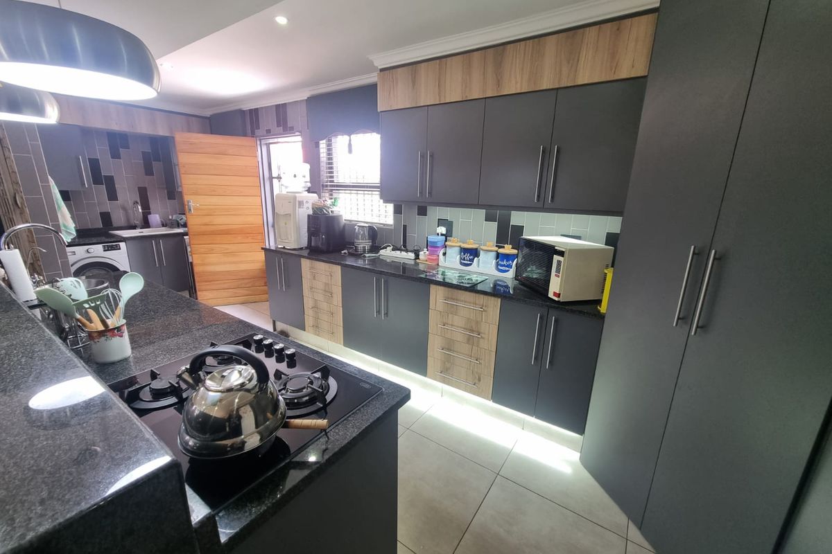 Modern kitchen featuring dark grey and wood-tone cabinetry, granite countertops, a gas hob, and integrated lighting, with an adjacent scullery area.