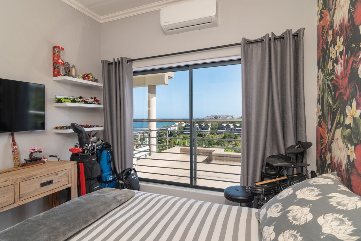 A bedroom featuring a sliding glass door leading to a balcony with coastal views, equipped with a wall-mounted air conditioning unit.
