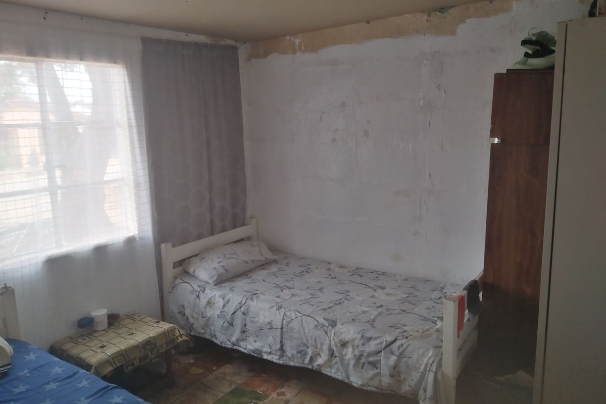 A bedroom featuring a window with natural light, requiring cosmetic updates to the walls, ceiling, and flooring to improve its overall condition.