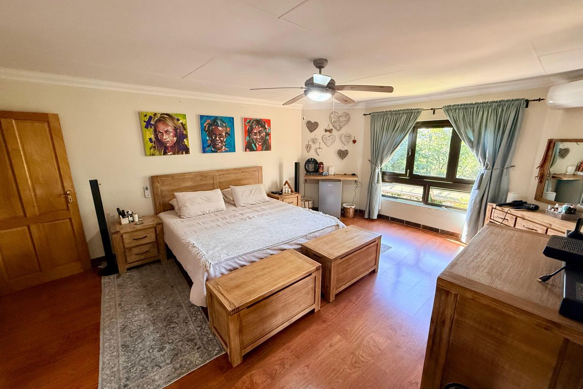 Spacious bedroom featuring wood-look laminate flooring, a ceiling fan, and large windows providing natural light.