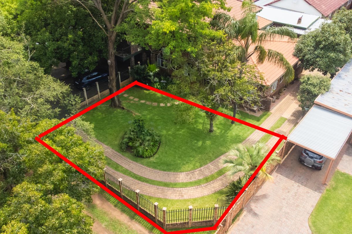 Aerial view of the property highlighting the landscaped front garden, paved walkways, perimeter fencing, and a covered carport area.