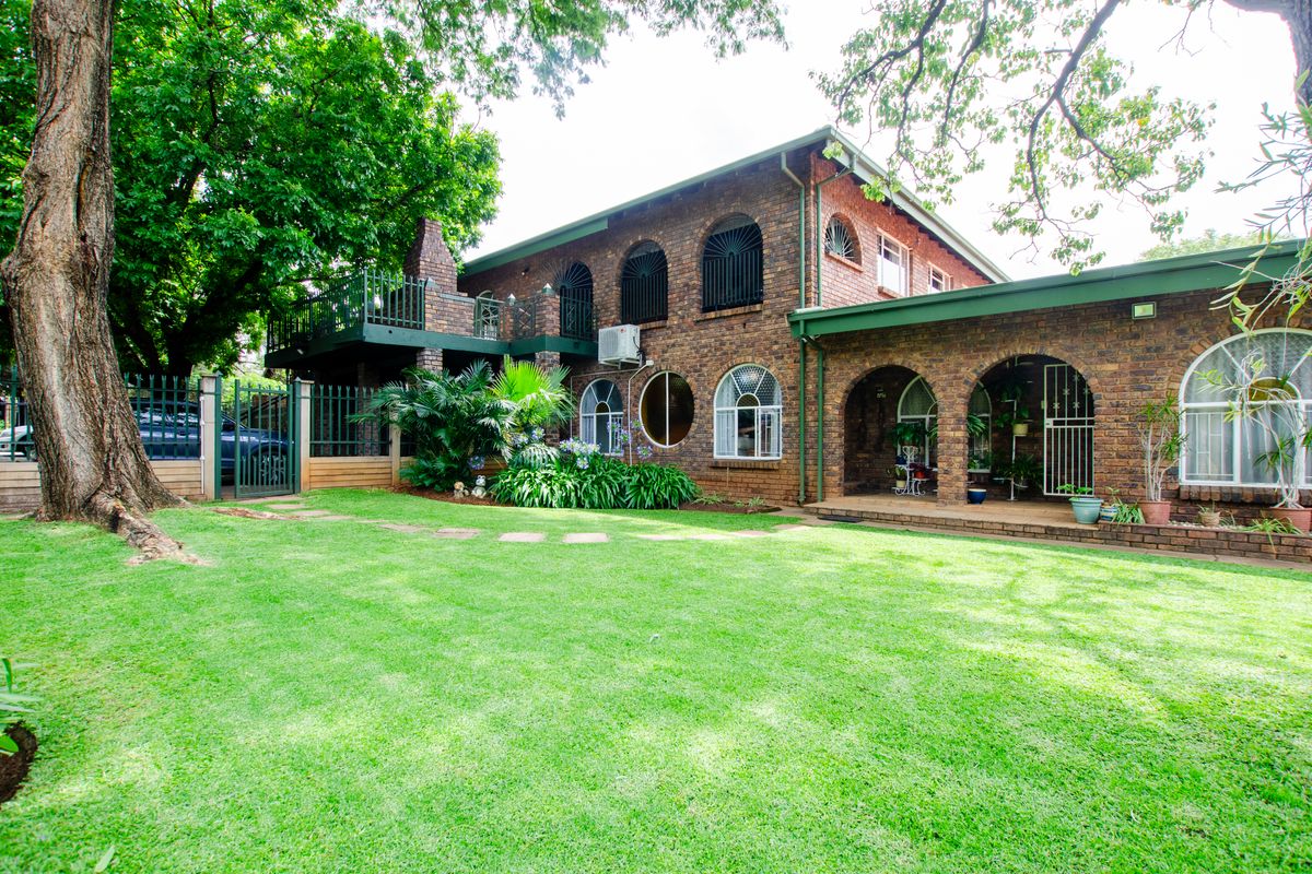 A spacious rear exterior view of a double-story face-brick house featuring arched windows, a covered patio, and a well-maintained garden.