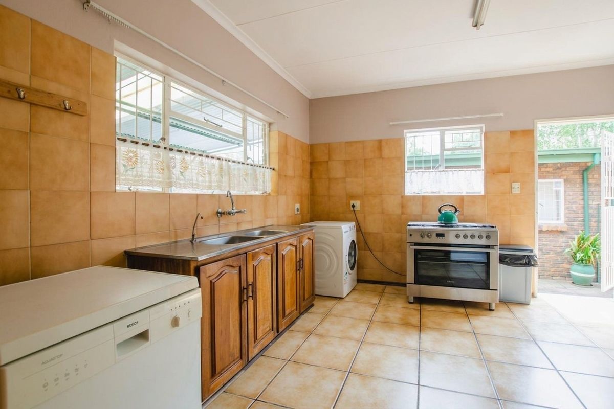 Functional kitchen featuring wooden cabinetry, stainless steel sink, tiled splashbacks, and a freestanding oven, with direct access to the rear exterior.