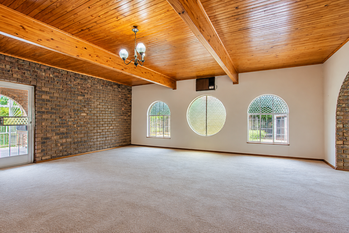 Spacious living area featuring a high timber-clad ceiling, exposed brick wall, and unique arched and circular windows, providing a bright and character-filled space.