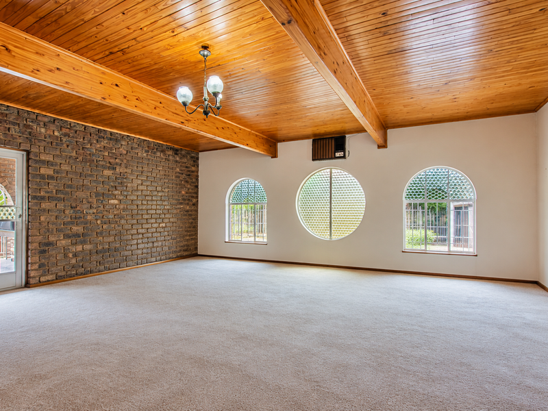 Spacious living area featuring a high timber-clad ceiling, exposed brick wall, and unique arched and circular windows, providing a bright and character-filled space.