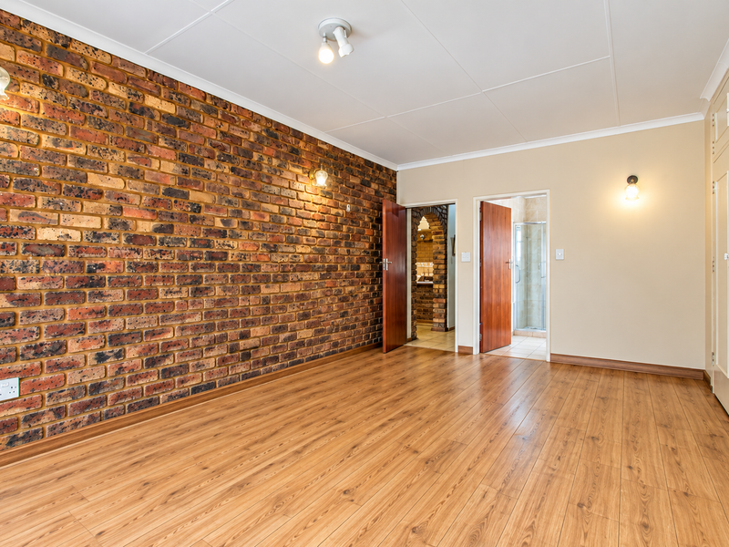 Spacious bedroom featuring an exposed brick accent wall, laminate flooring, and extensive built-in cupboard storage, with direct access to an en-suite bathroom.