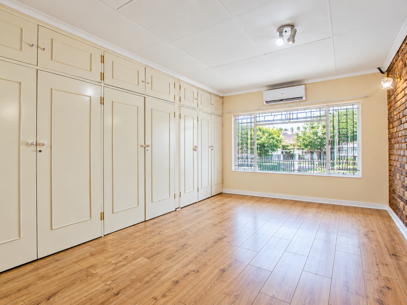 Spacious bedroom featuring extensive built-in cabinetry, warm laminate flooring, an exposed brick feature wall, and a split-system air conditioner for climate control.