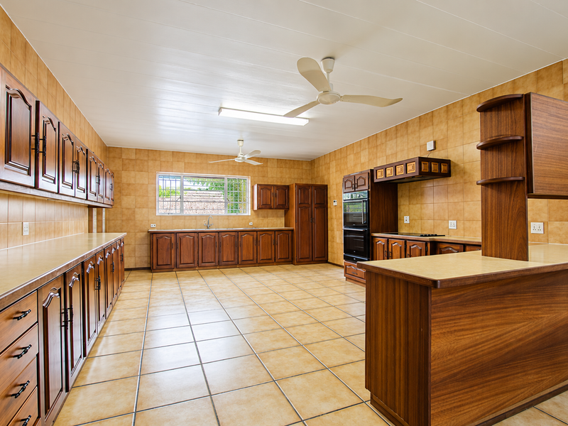 Spacious kitchen featuring extensive wooden cabinetry, tiled surfaces, a built-in double oven, and a breakfast bar, offering a functional and well-maintained layout.