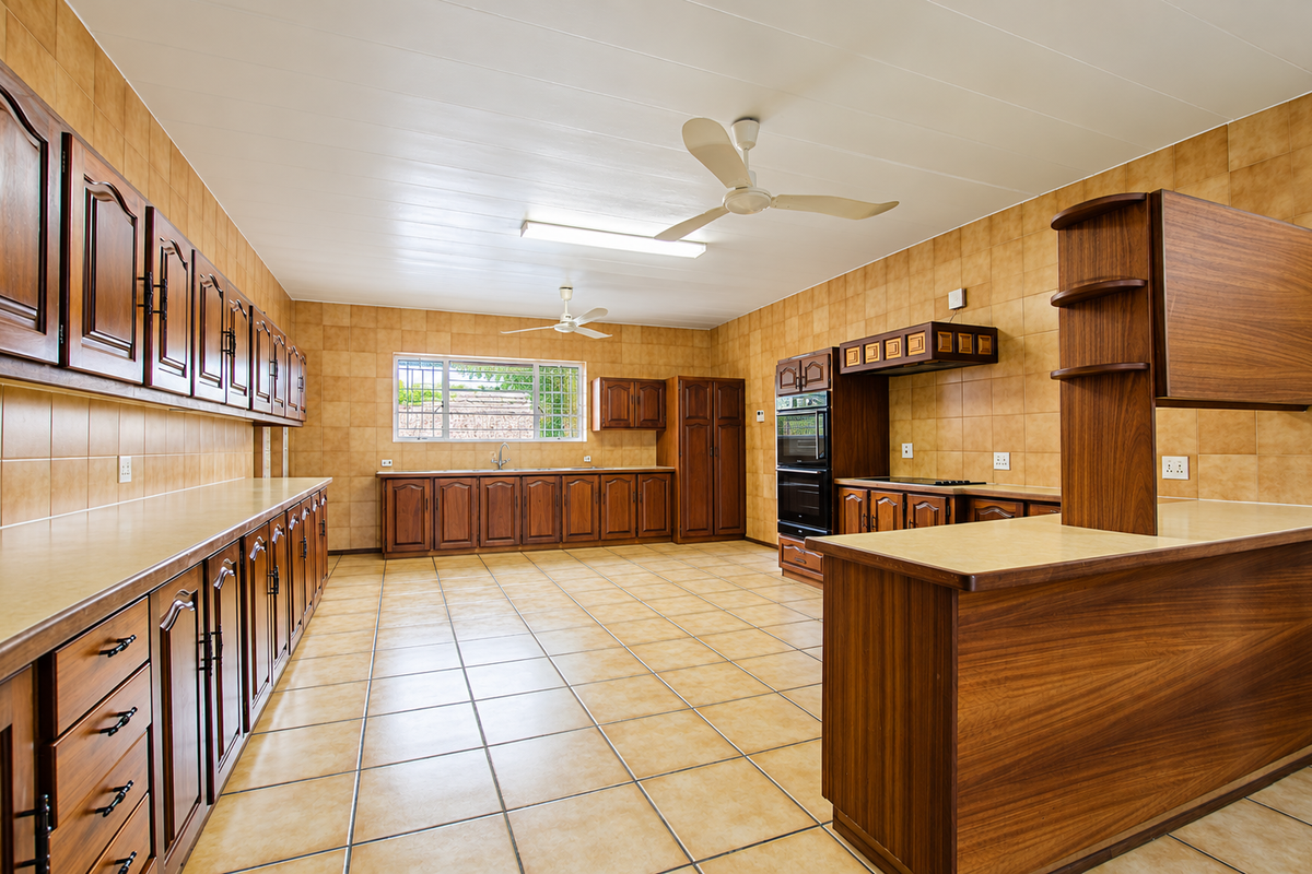 Spacious kitchen featuring extensive wooden cabinetry, tiled surfaces, a built-in double oven, and a breakfast bar, offering a functional and well-maintained layout.