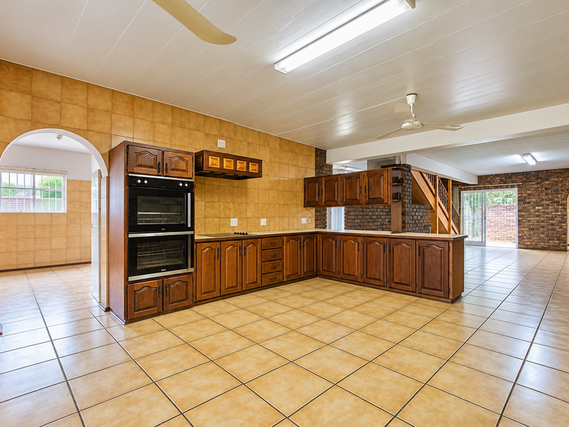 Spacious open-plan kitchen and living area featuring tiled flooring, exposed brick accents, built-in double oven, and direct access to the rear outdoor space.