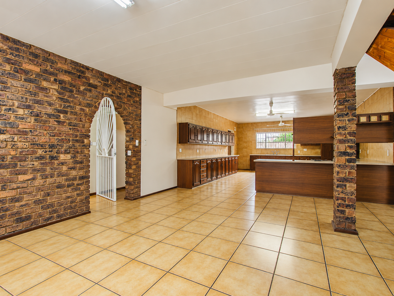 Spacious open-plan living and kitchen area featuring exposed brick accents, ceramic tile flooring, and extensive wooden cabinetry throughout the kitchen space.