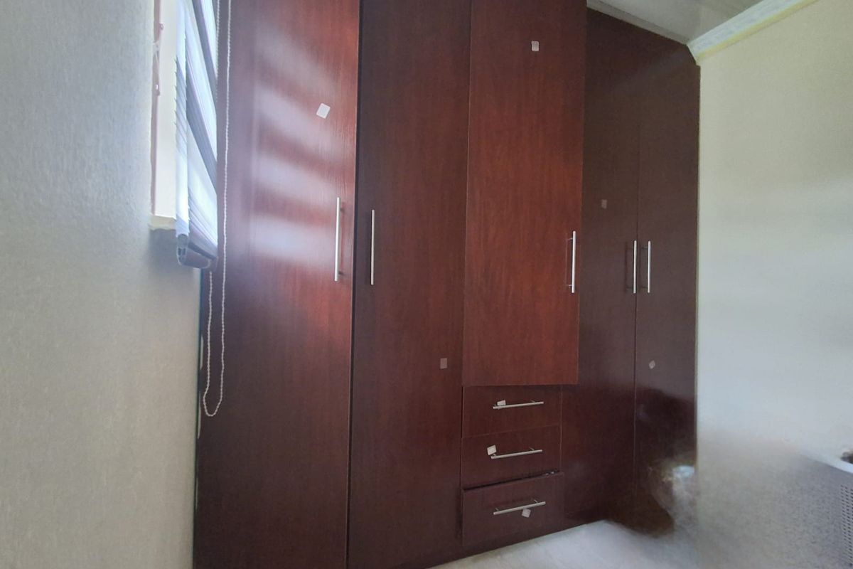 A bedroom featuring built-in dark wood cabinetry with integrated drawers and hanging space, complemented by a window with a fitted roller blind.