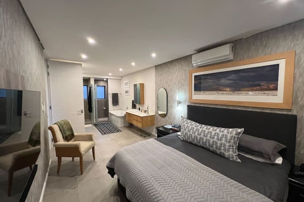 Spacious bedroom featuring an integrated open-plan bathroom with a floating vanity, freestanding bathtub, glass shower, and modern recessed lighting.