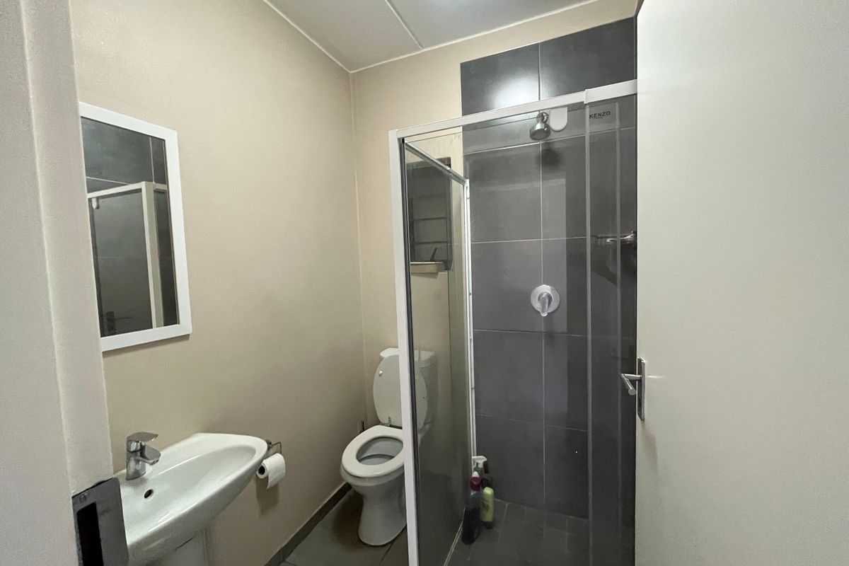 A functional bathroom featuring a pedestal basin, toilet, and a glass-enclosed shower with dark tiled accents.