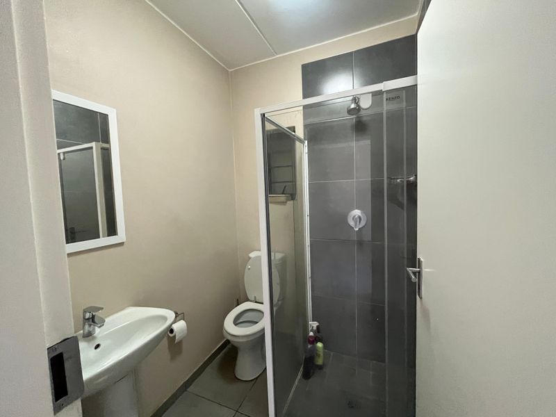 A functional bathroom featuring a pedestal basin, toilet, and a glass-enclosed shower with dark tiled accents.