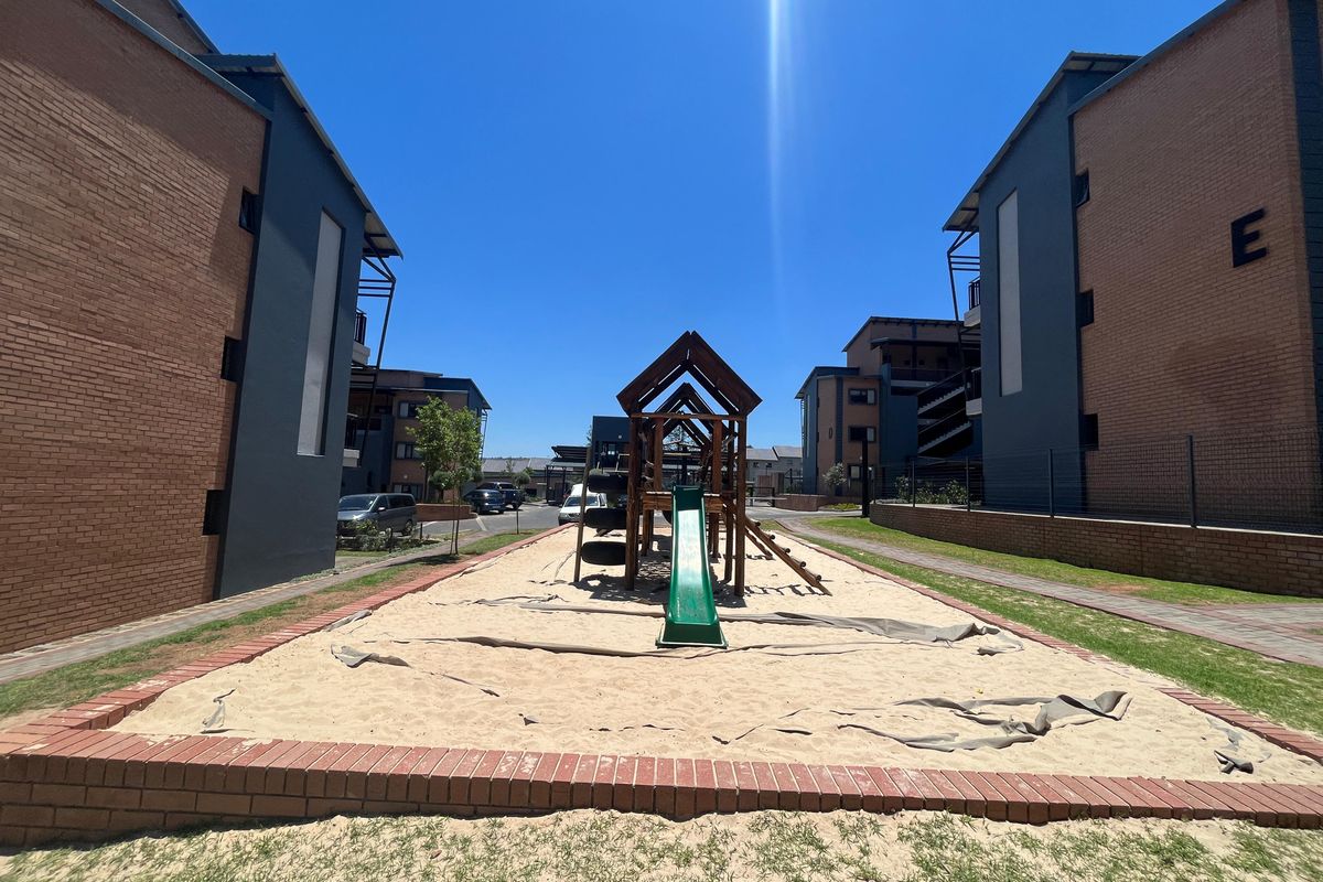 Communal outdoor area featuring a playground with a sand pit situated between apartment blocks with brick and rendered facades.