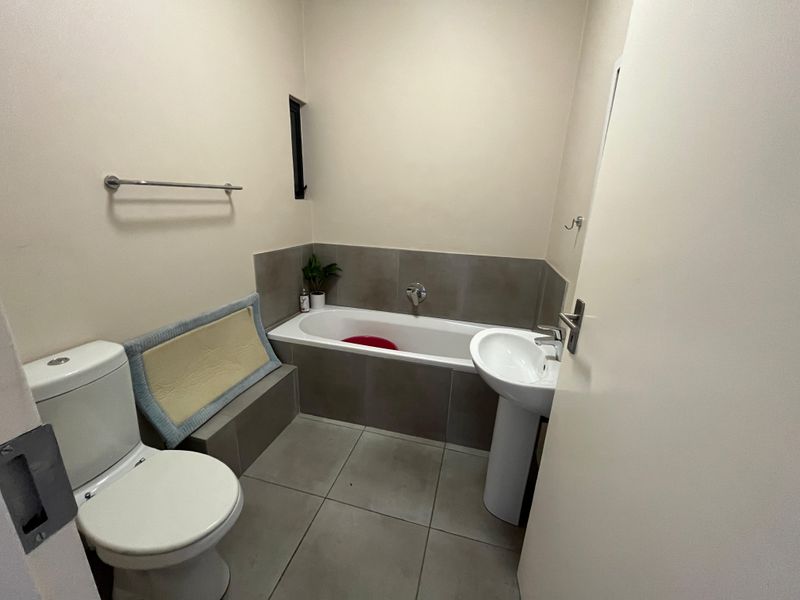 A functional bathroom featuring a bathtub with tiled surround, pedestal basin, and toilet, finished with neutral wall paint and floor tiles.