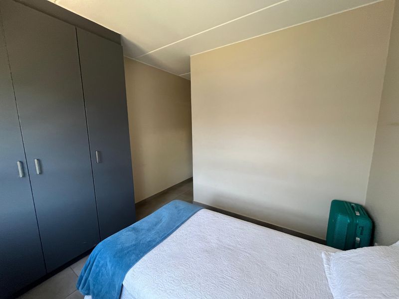 A bedroom featuring neutral wall tones, tiled flooring, and a dark grey built-in wardrobe providing ample storage space.
