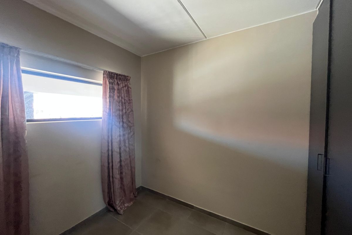 A simple, empty bedroom featuring tiled flooring and a built-in wardrobe, offering a neutral canvas for personalization.
